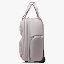 Side view of 16-inch underseat carry-on luggage with wheels, showing a slim profile, smooth-rolling wheels, and multiple zippered side pockets. #show #color_grey-pink