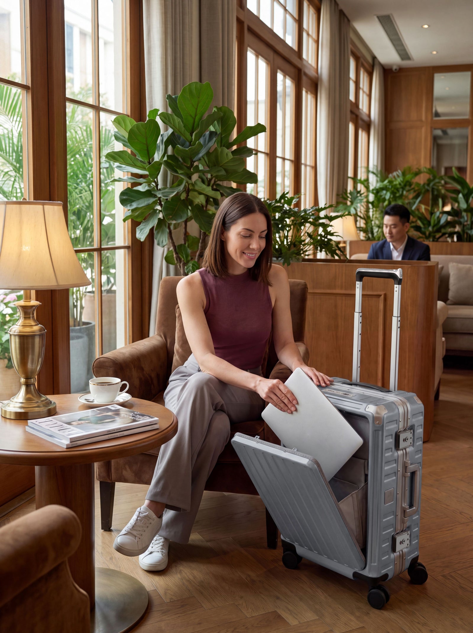 Woman taking out laptop from front pocket of silver aluminum carry-on luggage in hotel lounge.#color_sliver_grey