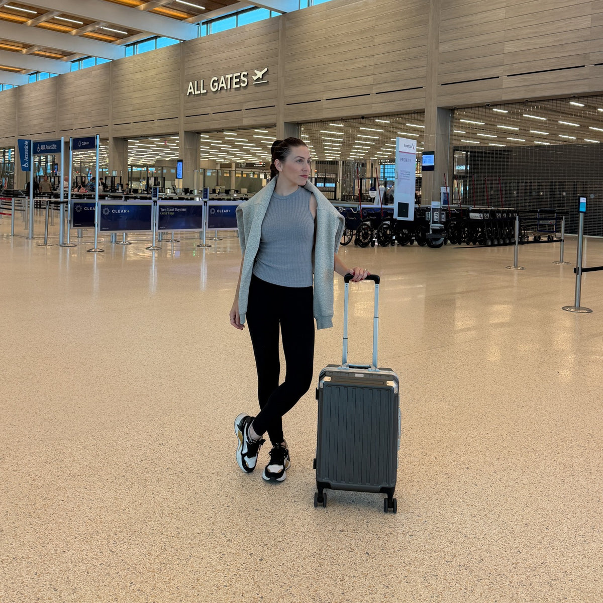 Traveler in an airport terminal with a gray LUGGEX aluminum-frame carry-on spinner suitcase.#color_charcoal
